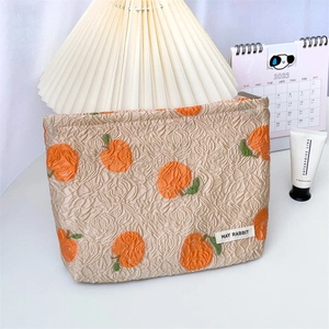 Detailed macro view of beige jacquard makeup bag with orange pattern and brand label