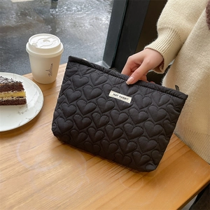 Close-up of black quilted heart pattern on cotton cosmetic bag with brand label detail