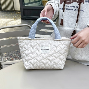 Detail of white quilted heart pattern and light blue handle on a small tote bag