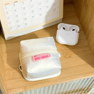 Detail of a fluffy white tent-shaped headphone case with a pearl charm on wooden shelf
