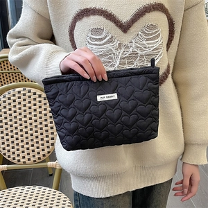 Detail of black quilted heart clutch bag with MAY RABBIT label held by a model