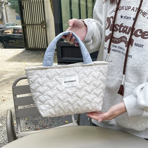 White quilted heart tote bag with blue handles held by hand to show size and texture