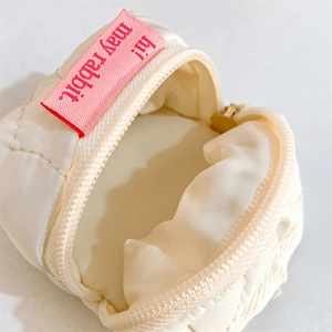 Detail shot of mini off-white quilted pouch with pink tag and metallic zipper closure