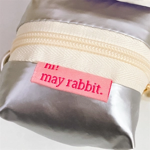 Macro shot of silver metallic pouch showing zipper detail and pink woven logo label