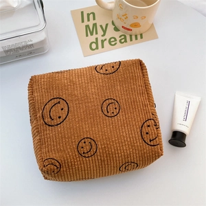 Top view of a brown corduroy makeup bag with embroidered smiley face on a desk