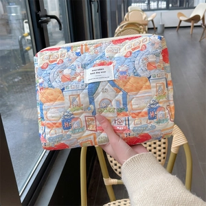 Close-up of quilted floral cosmetic bag with cartoon town print and woven brand label
