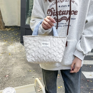 Quilted heart tote bag in cream with light blue handles shown in an outdoor lifestyle setting
