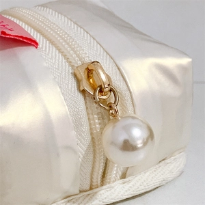 Detail of white satin earphone pouch with faux pearl zipper pull and gold hardware