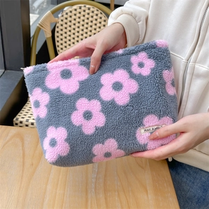 Detail of soft plush cosmetic bag with floral patterns and zipper closure held by hand