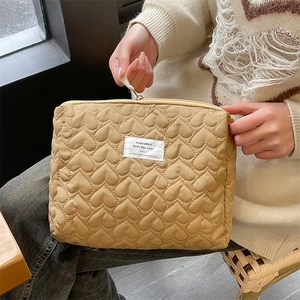 Detailed close-up of yellow heart-quilted cosmetic bag held by a model for size