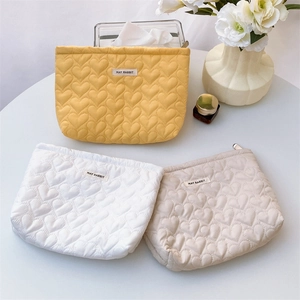Quilted heart cosmetic bags in yellow, white, and beige on a stylish table setup