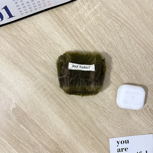 Detail van mosgroene pluche oortelefoonhoes met merklabel op houten oppervlak