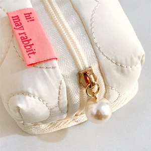 Detail of white quilted storage pouch featuring a pearl zipper pull and pink brand label