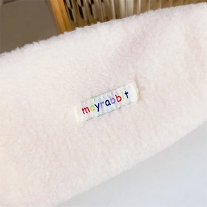 Detailed macro view of white plush fabric and colorful mayrabbit embroidered brand label