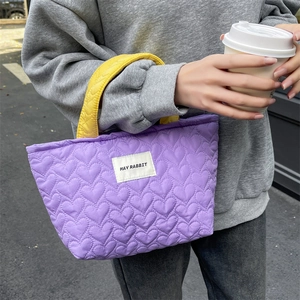 Detail of purple quilted heart handbag featuring vibrant yellow handles and brand label