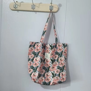 Détail du cabas en toile à fleurs roses sur tissu bleu avec étiquette blanche cousue