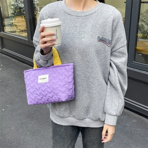 Detail of purple heart-quilted handbag with yellow handles and brand label