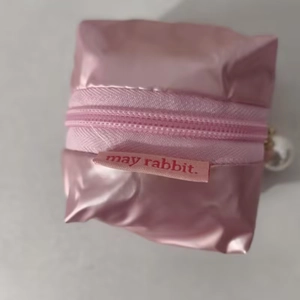 Detail of pink satin storage pouch featuring a zipper and an elegant pearl pendant charm