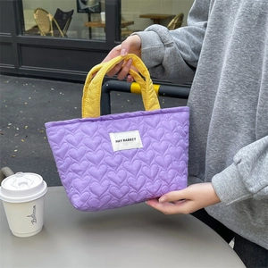 Detail of purple heart-quilted handbag with brand tag and yellow handles in casual scene