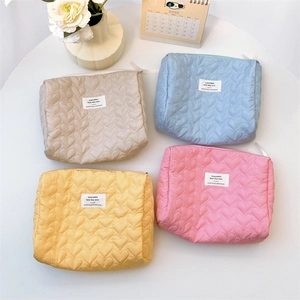 Quilted heart pattern makeup bags in beige, blue, yellow, and pink colors on a white table