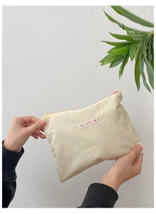 Hand holding a cream fabric makeup pouch with pink zipper and hi jolly label