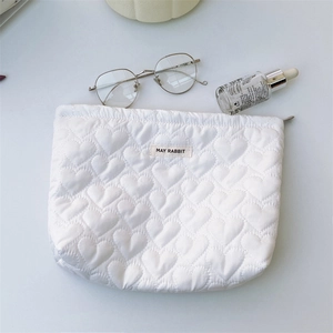 Detailed close-up of white heart-quilted toiletry bag with zipper and May Rabbit label
