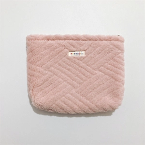 Detailed close-up of a pink plush cosmetic bag with diagonal quilted texture and woven label