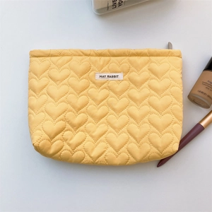 Detail of yellow quilted heart pattern cosmetic bag with metal zipper and logo tag