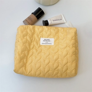 Close-up of yellow quilted heart pattern makeup bag with a minimalist woven brand label