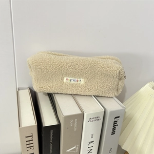 Detail of soft off-white plush pencil case with embroidered colorful brand label