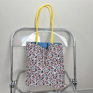 Detail of floral tote bag with yellow handles and blue lining on a modern clear chair