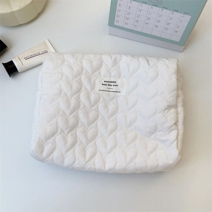 Close-up of white quilted heart pattern makeup bag with branded label on desk