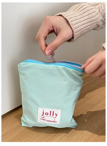Détail de la pochette en tissu vert menthe avec zip violet et étiquette tissée blanche