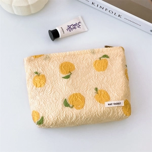 Detail of cream jacquard makeup bag with yellow citrus pattern and brand label