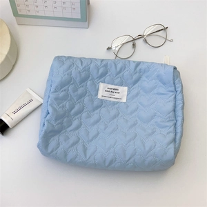 Close-up of light blue quilted cosmetic bag with heart pattern and minimalist branding