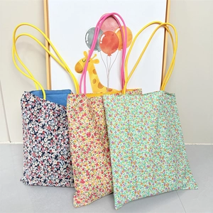 Three floral canvas tote bags in navy, yellow, and green with vibrant slim handles