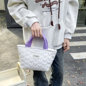 Close-up of heart-quilted white tote bag with purple handles and branded woven label