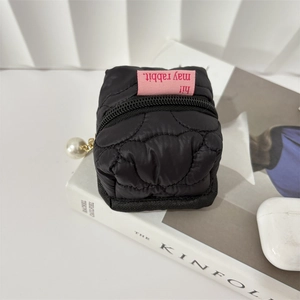 Quilted black mini pouch with pearl zipper detail shown on a magazine next to earbuds