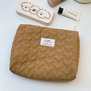 Detailed view of caramel heart-quilted cosmetic bag with branded woven label and zipper tape