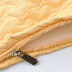 Macro shot of heart quilted stitching and smooth metal zipper on a pale yellow makeup bag
