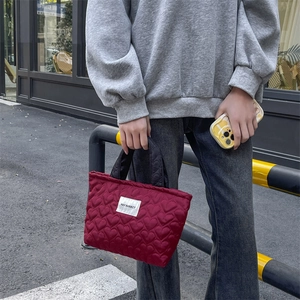 Close-up of wine red quilted handbag with heart patterns and black contrast handles