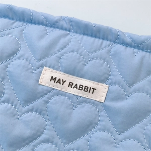Detail of light blue quilted heart fabric with a white May Rabbit woven brand label