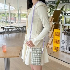 Green checkered mini phone bag with purple strap shown on a model in a bright cafe setting