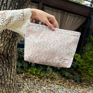 Detail of floral makeup bag with MAY RABBIT label held against white crochet knit background
