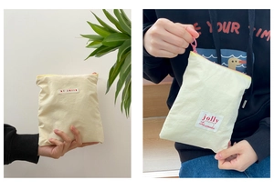 Gros plan d'une trousse à maquillage en toile crème tenue à la main avec fermeture