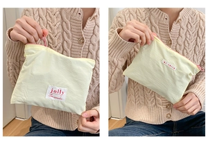 Detailed close-up of light yellow macaron makeup bag with woven labels and pink zipper