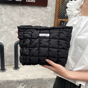 Detail of black quilted cosmetic bag with MAY RABBIT logo label held by hand