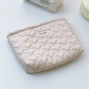 Detailed view of the heart-shaped quilted pattern and brand label on a cream makeup bag