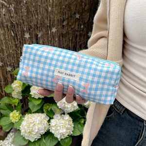 Blue and white checkered pencil case with pink bows held against a garden background