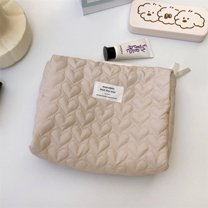 Close-up of beige quilted heart cosmetic bag with zipper and logo tag in a cozy setup